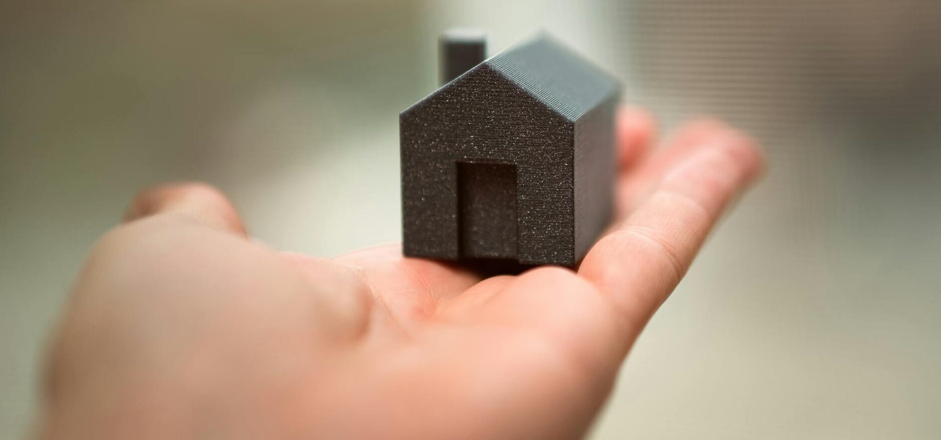 Close-up of a hand holding a miniature house model representing real estate concepts like buying or investment.